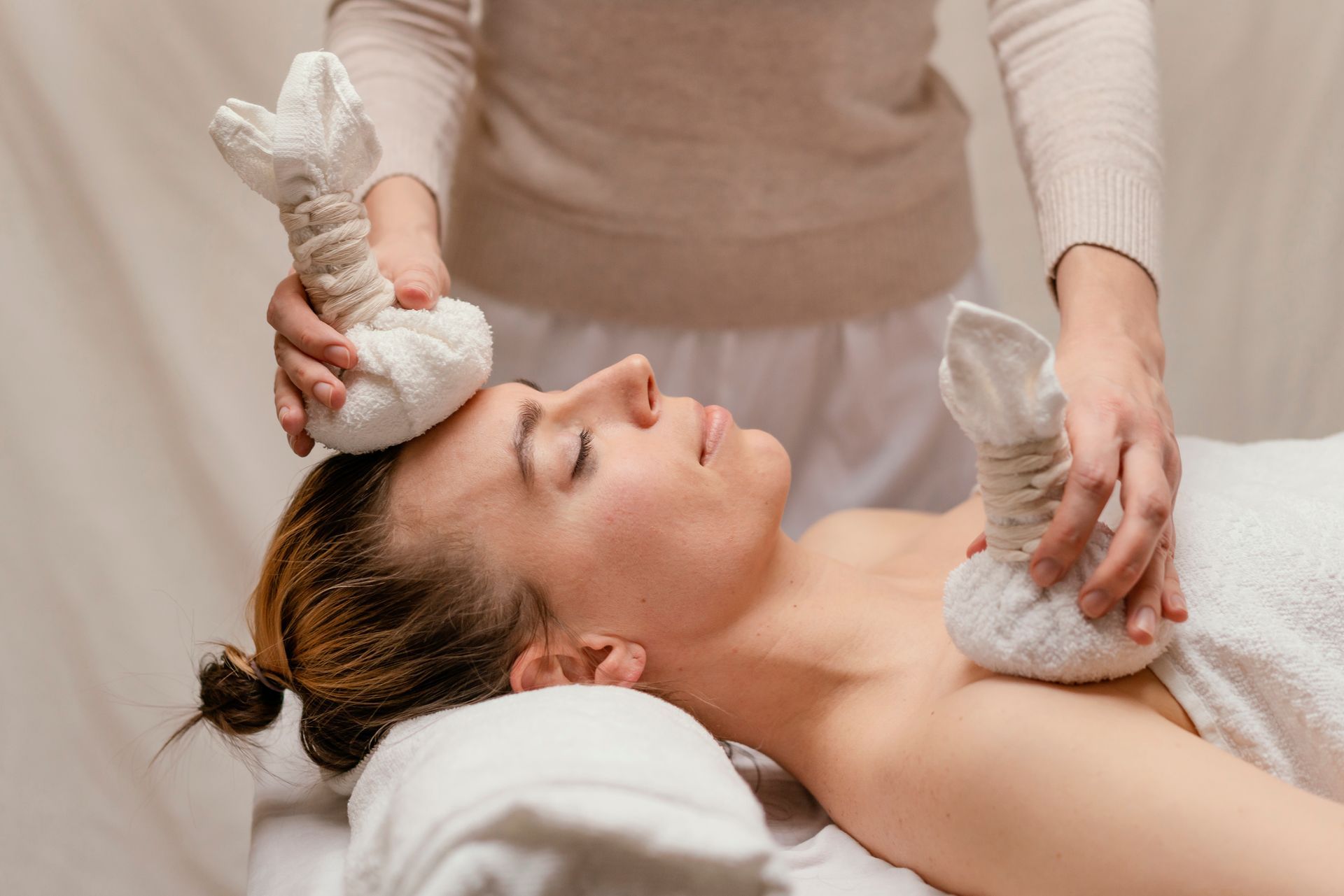 Spa therapist applying towel-wrapped stones to a woman receiving a facial treatment