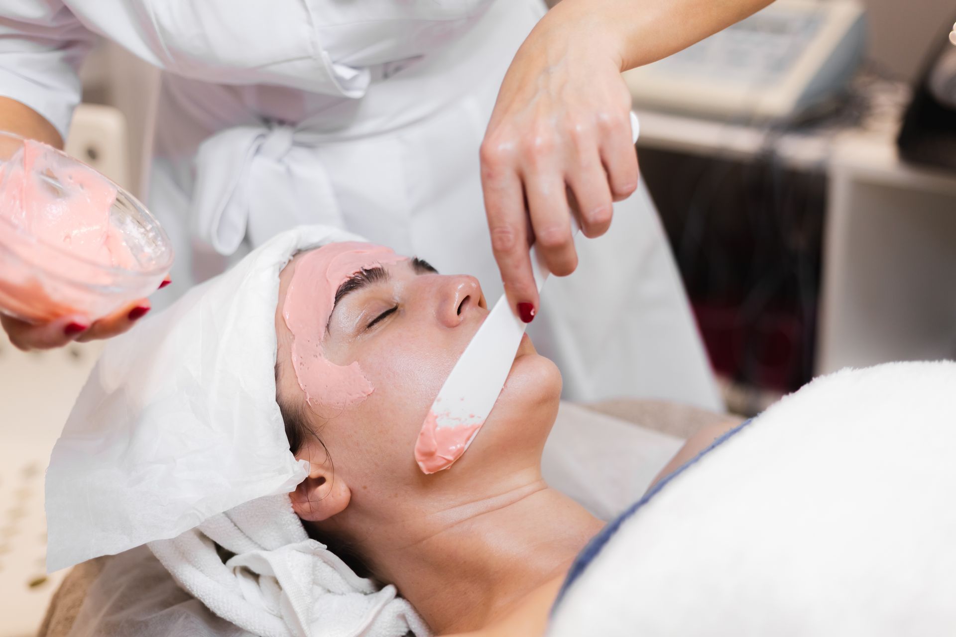 Facial spa treatment with a clinician applying cream to a woman’s face with a brush