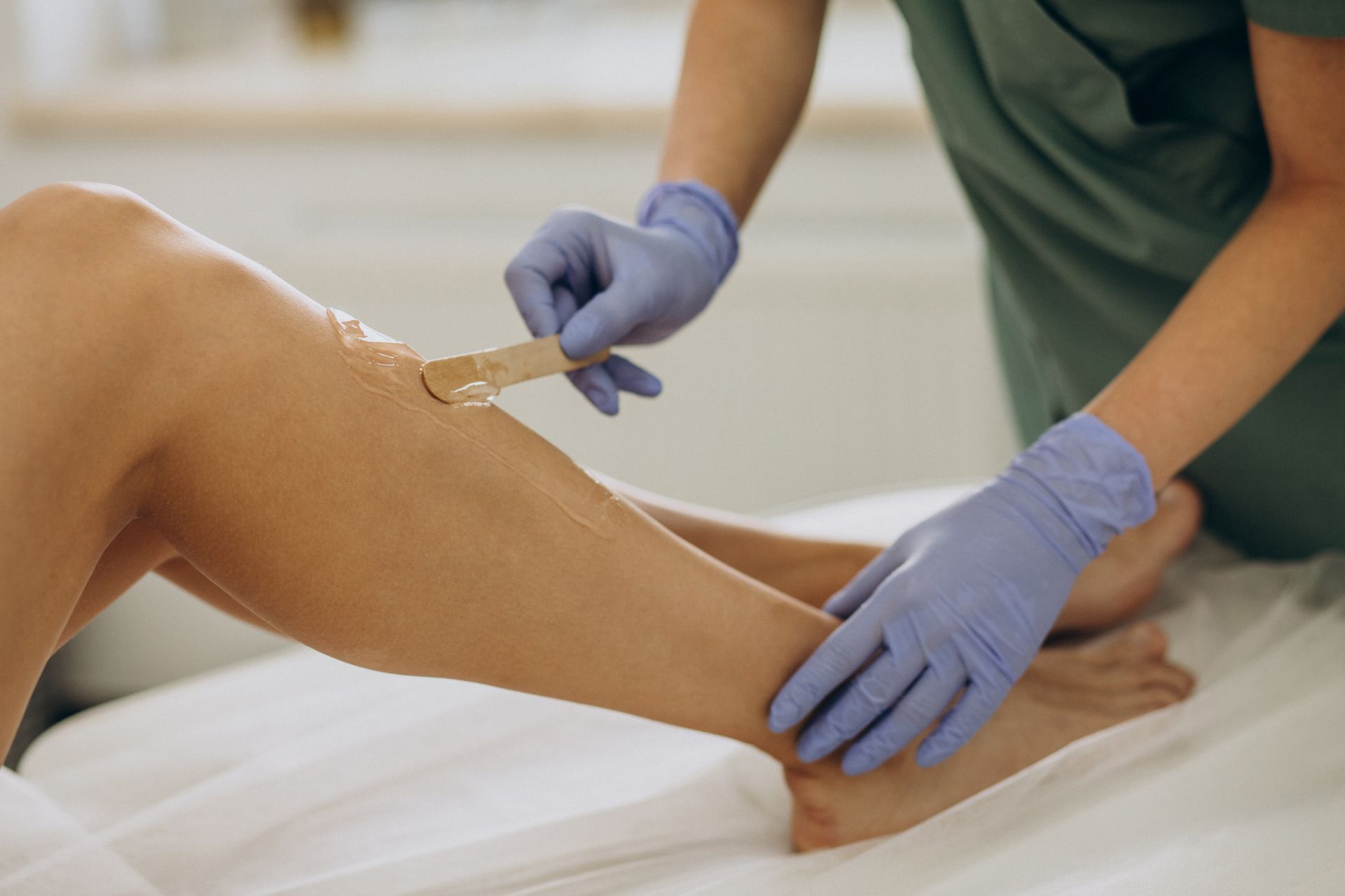 Gloved clinician waxing a person's leg on a treatment table