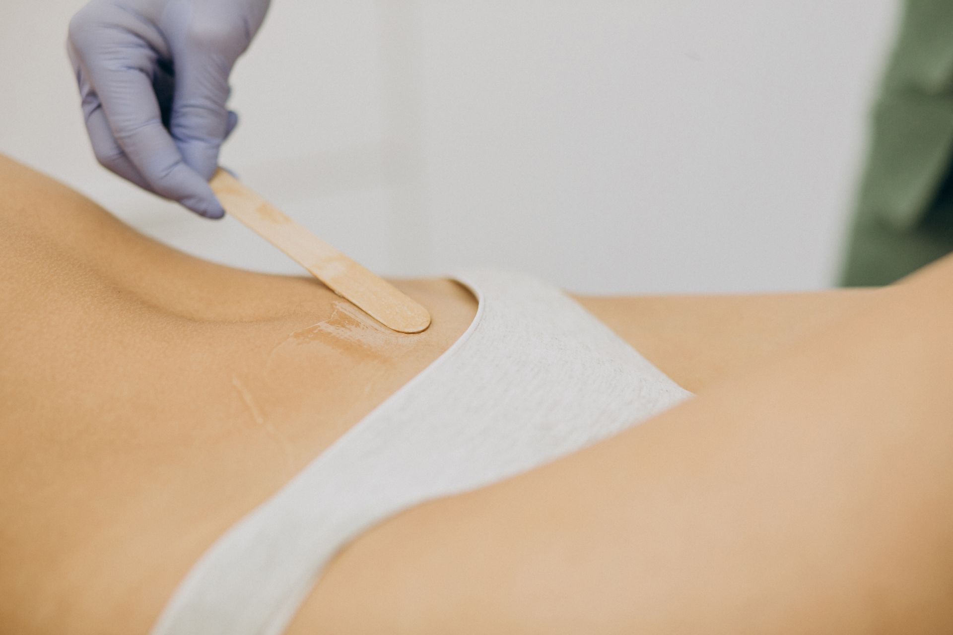 Gloved hand removing a wax strip from a person’s skin during waxing treatment