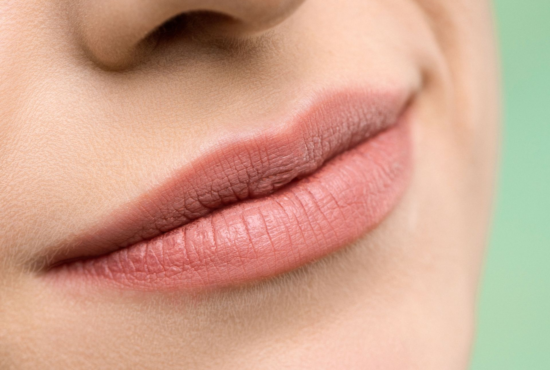 Close-up of smiling lips with soft pink lipstick on a blurred skin-toned background