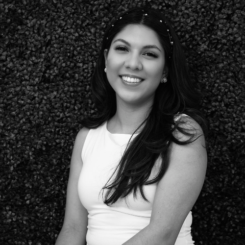 Smiling woman in a white sleeveless top against a leafy background