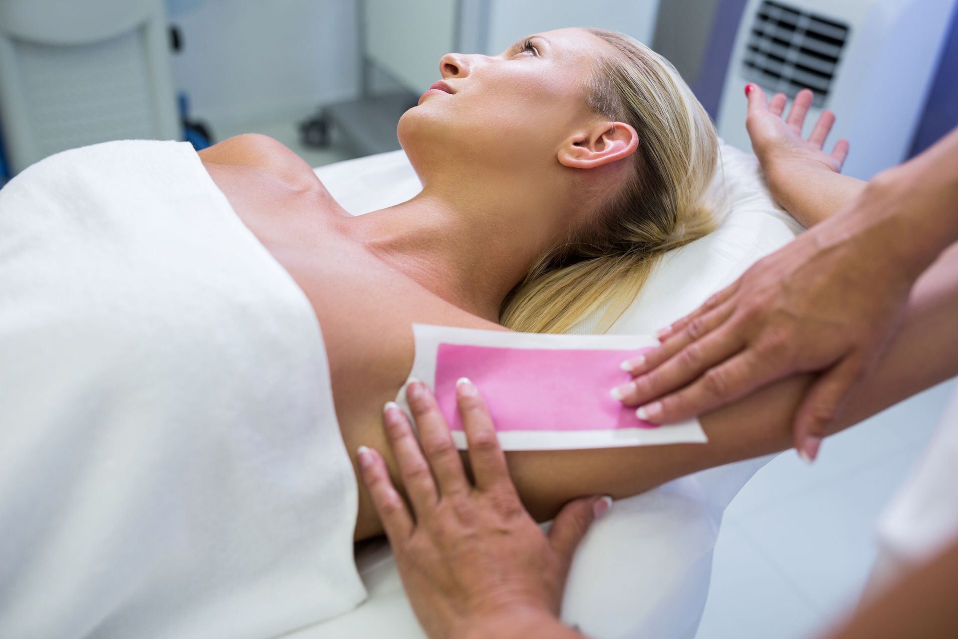 Woman receiving a pink wax strip treatment on her back in a spa setting