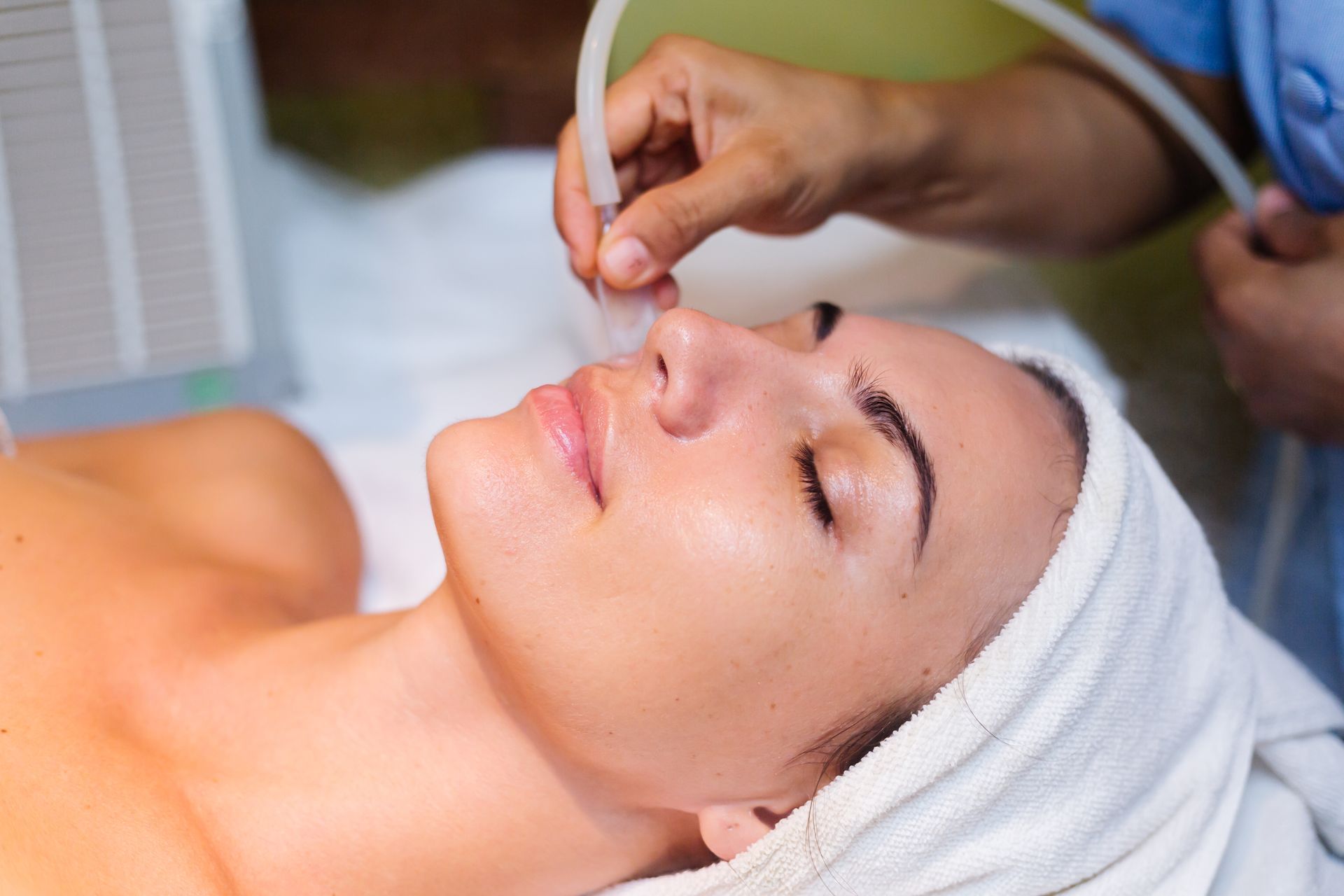 Woman receiving a facial treatment while lying on a spa bed with a towel wrapped around her head