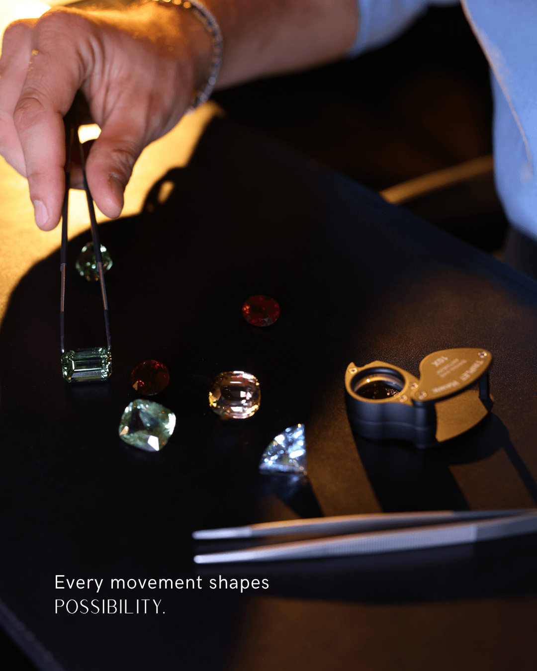 Hand using a baton over colorful dice and a gold ring on a black tray, with a notebook nearby