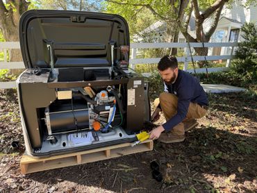 Man kneels beside an open generator with exposed wiring outdoors, adjusting a yellow cable.