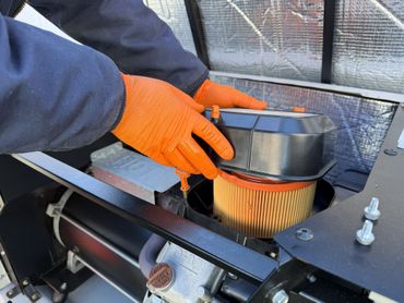 Orange-gloved hands installing an air filter in a vehicle engine compartment