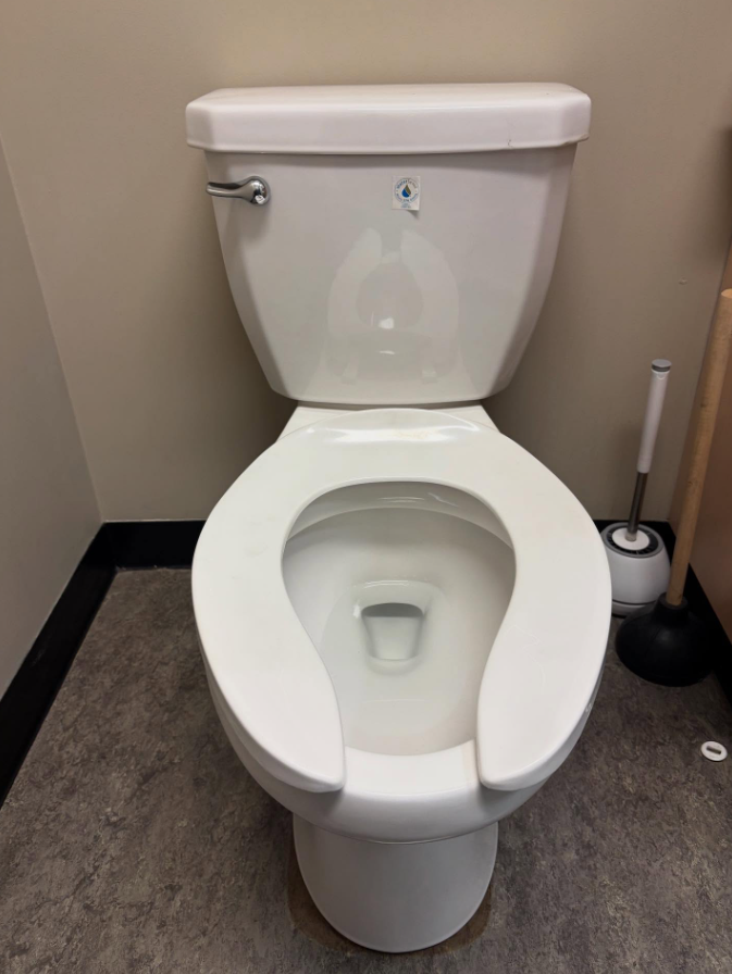 White toilet in a beige restroom stall with a toilet brush on the right side.