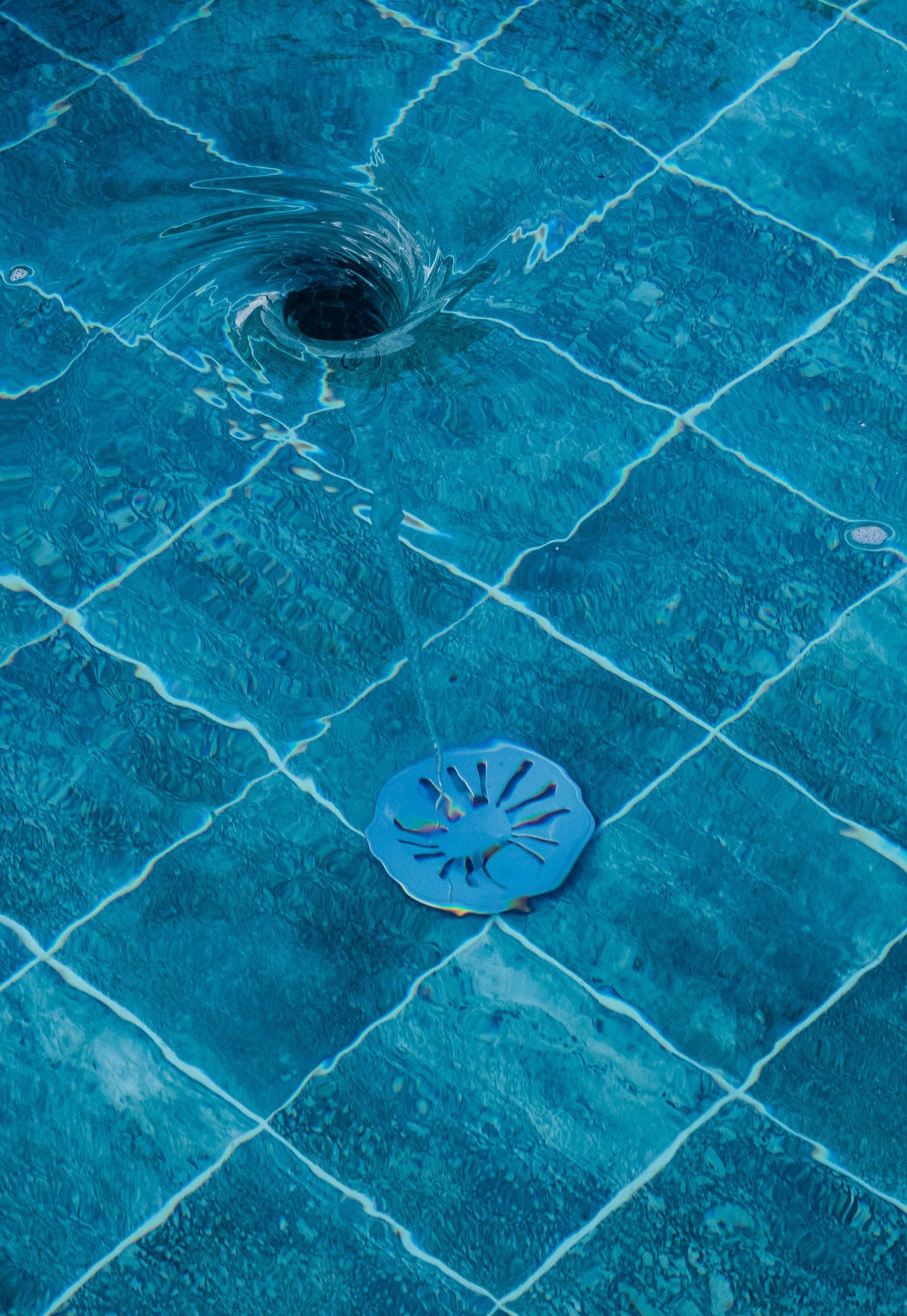 Blue-tiled pool drain with a small circular grate near a dark drain opening