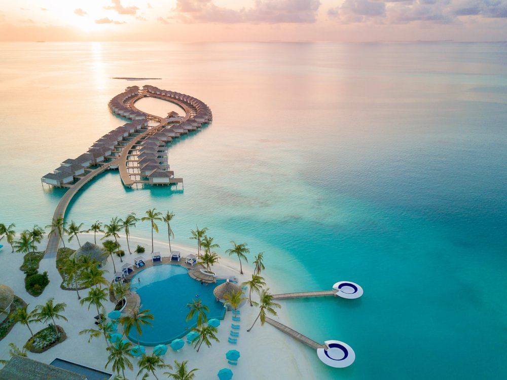 Aerial view of overwater bungalows and beach with turquoise water.