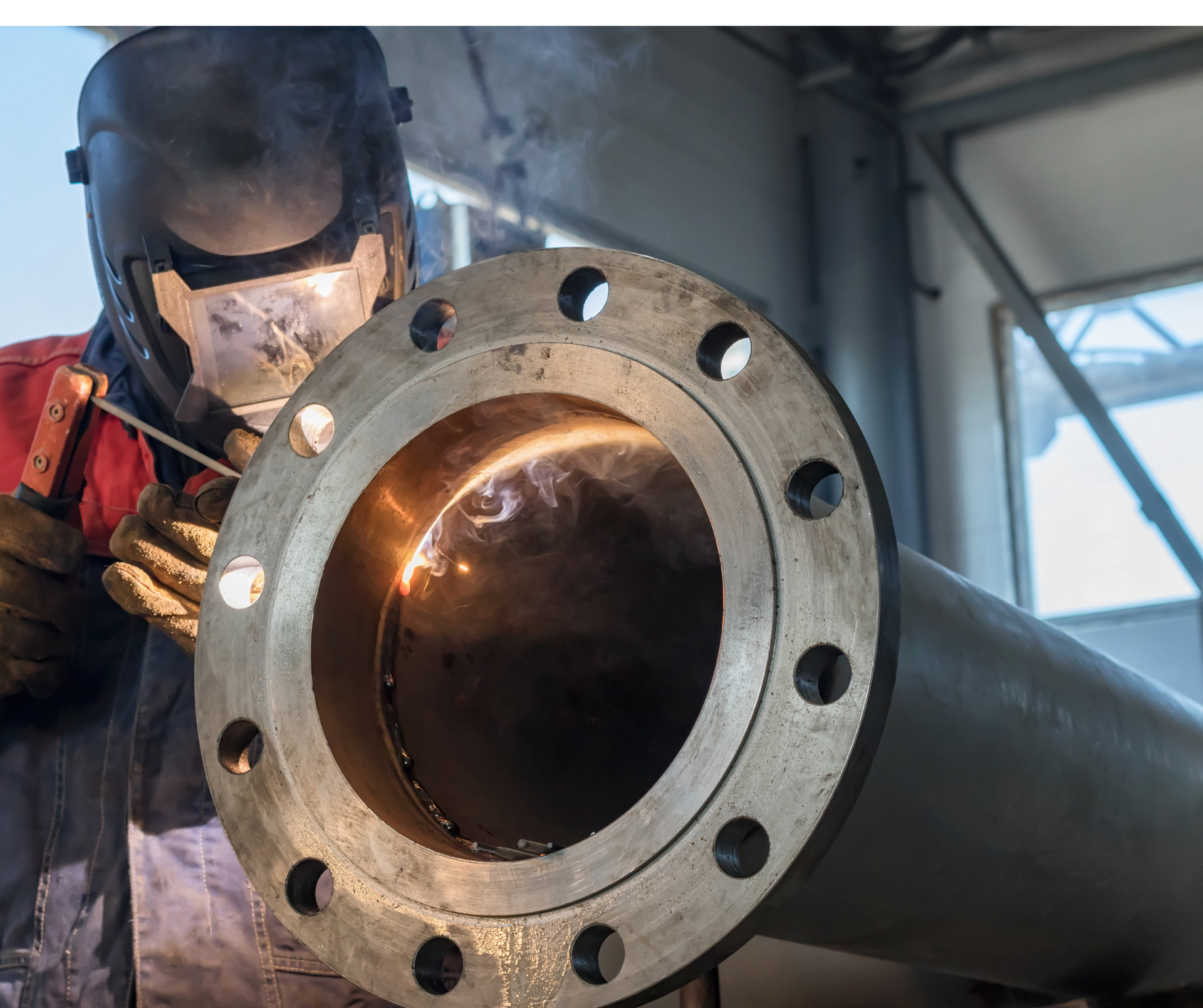 A man wearing a welding helmet is welding a piece of metal.
