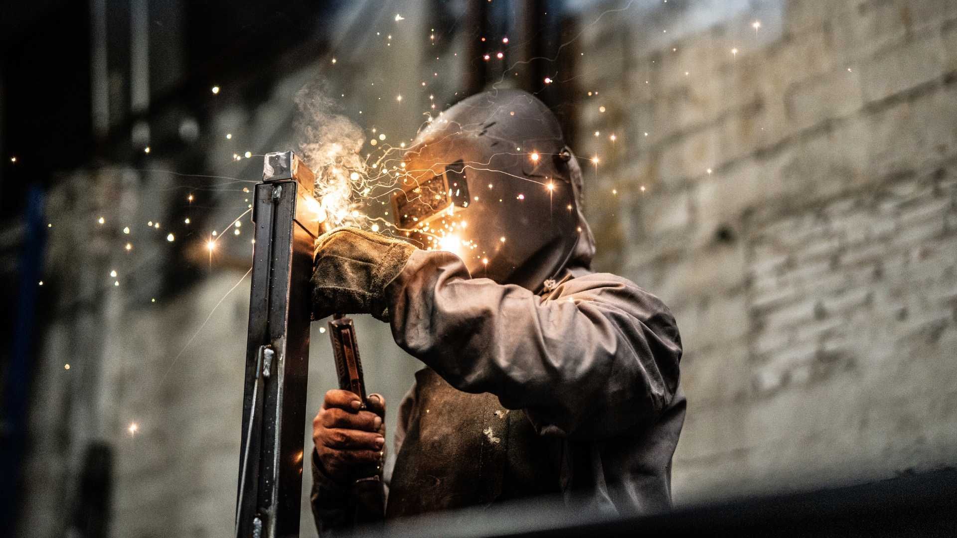 A man wearing a welding helmet is welding a piece of metal.