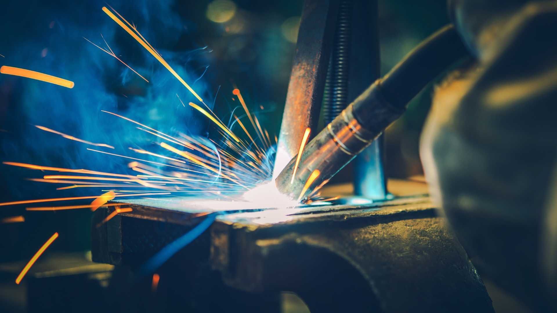 A person is welding a piece of metal in a factory.