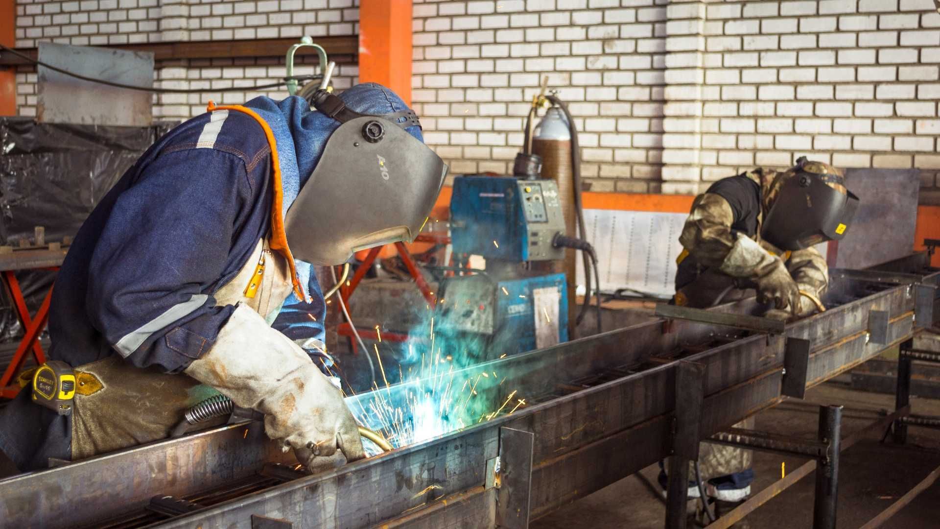 A man is welding a piece of metal in a factory.