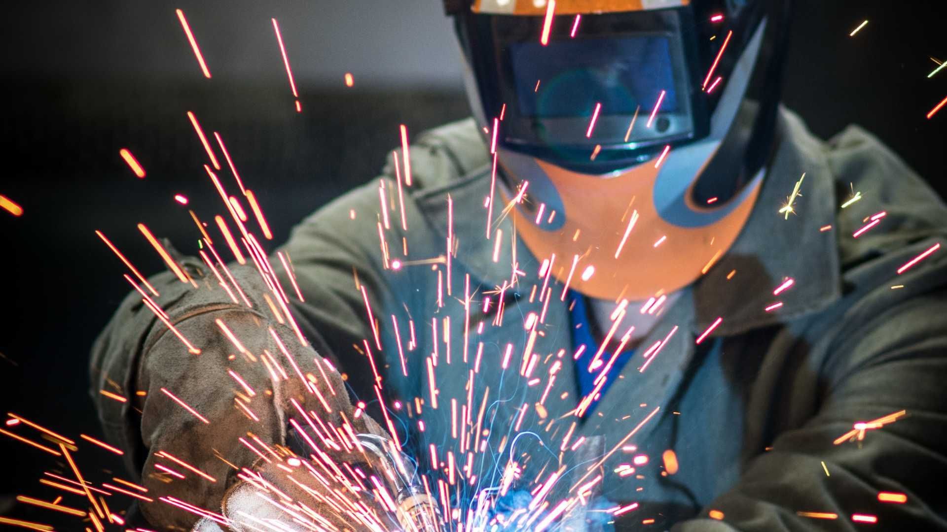 A man wearing a welding helmet is welding a piece of metal.