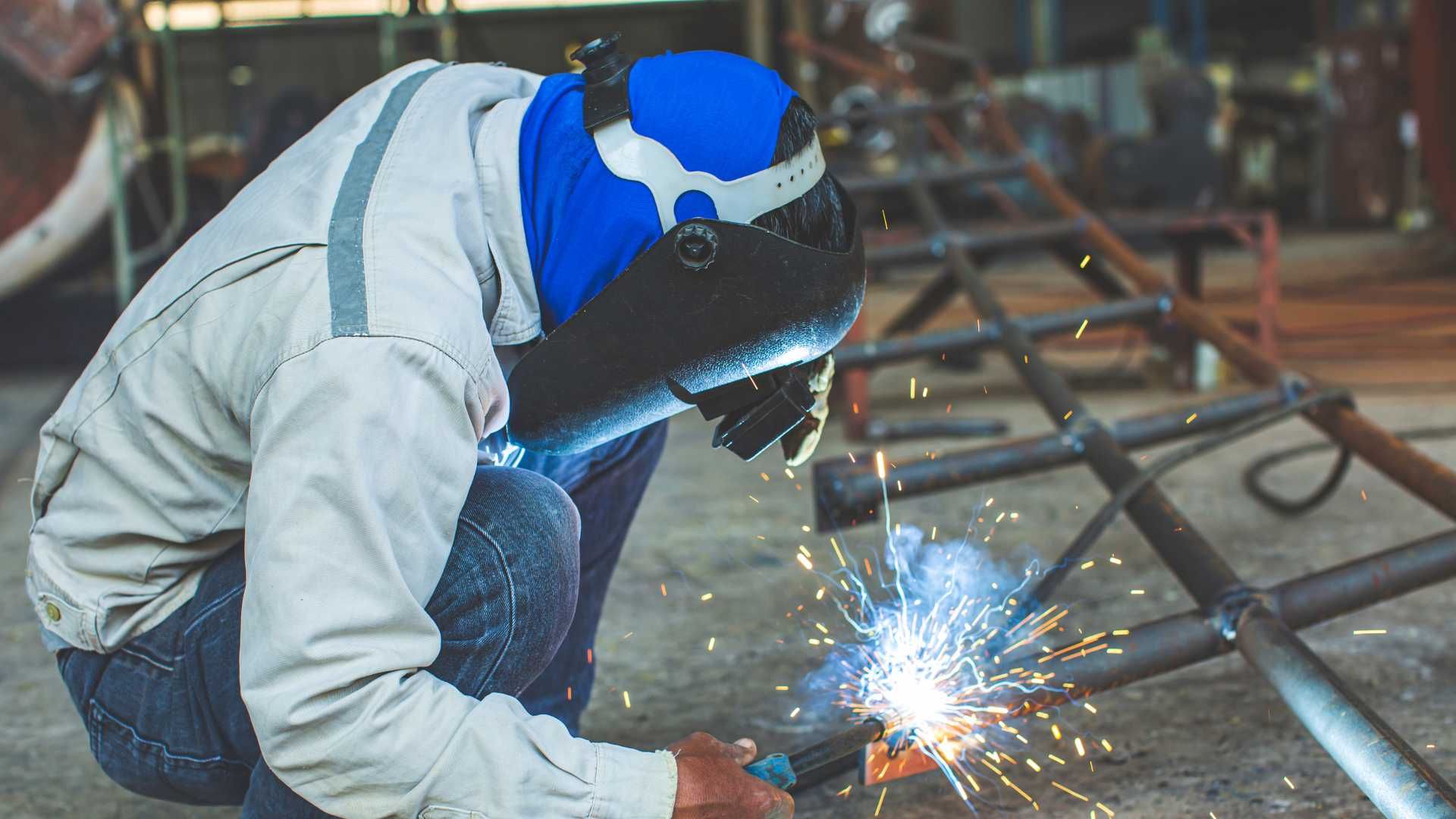 A man is welding a piece of metal in a factory.