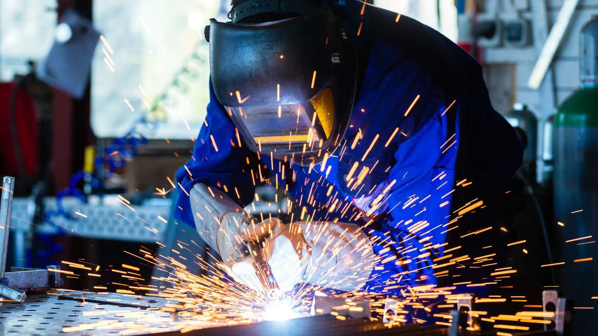 A man is welding a piece of metal in a factory.