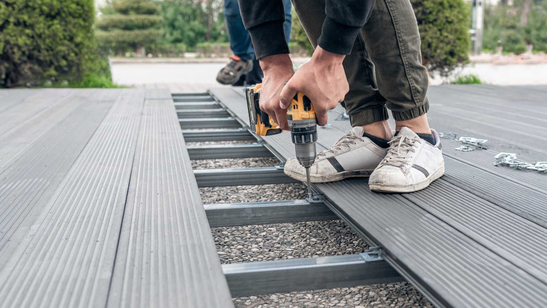 A man is using a drill to install a wooden deck.