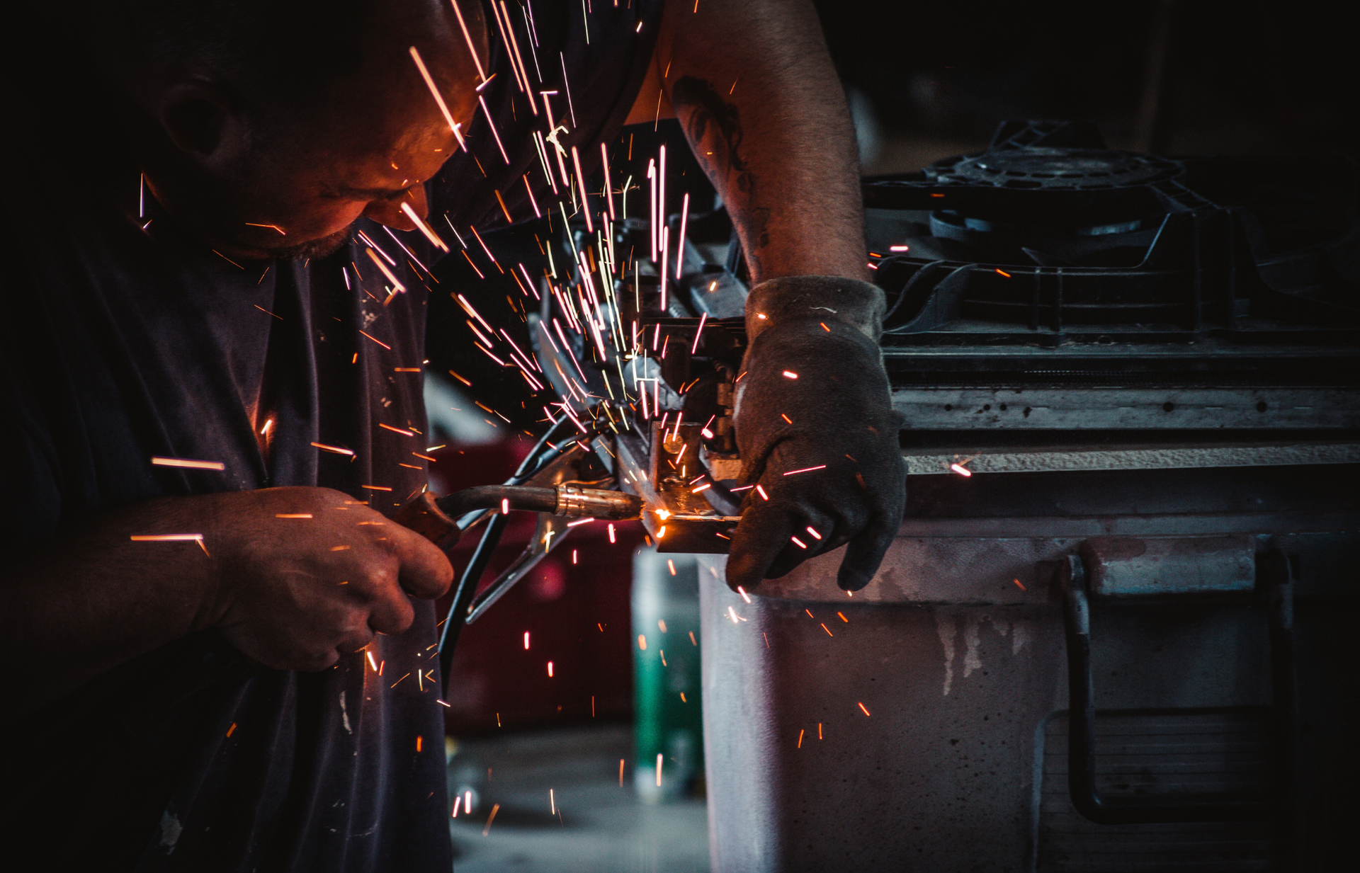 A man is welding a piece of metal in a dark room.