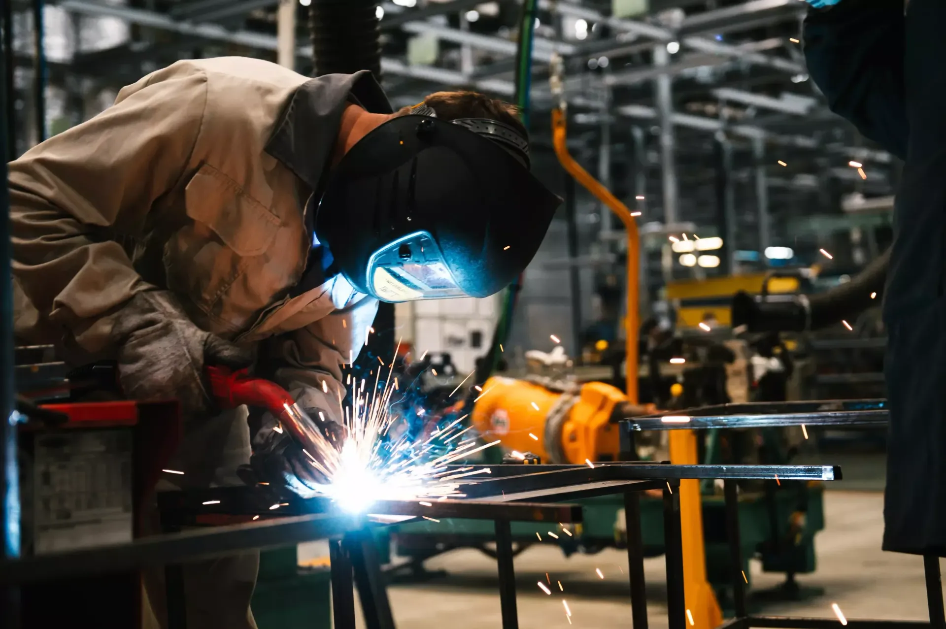 A man is welding a piece of metal in a factory.