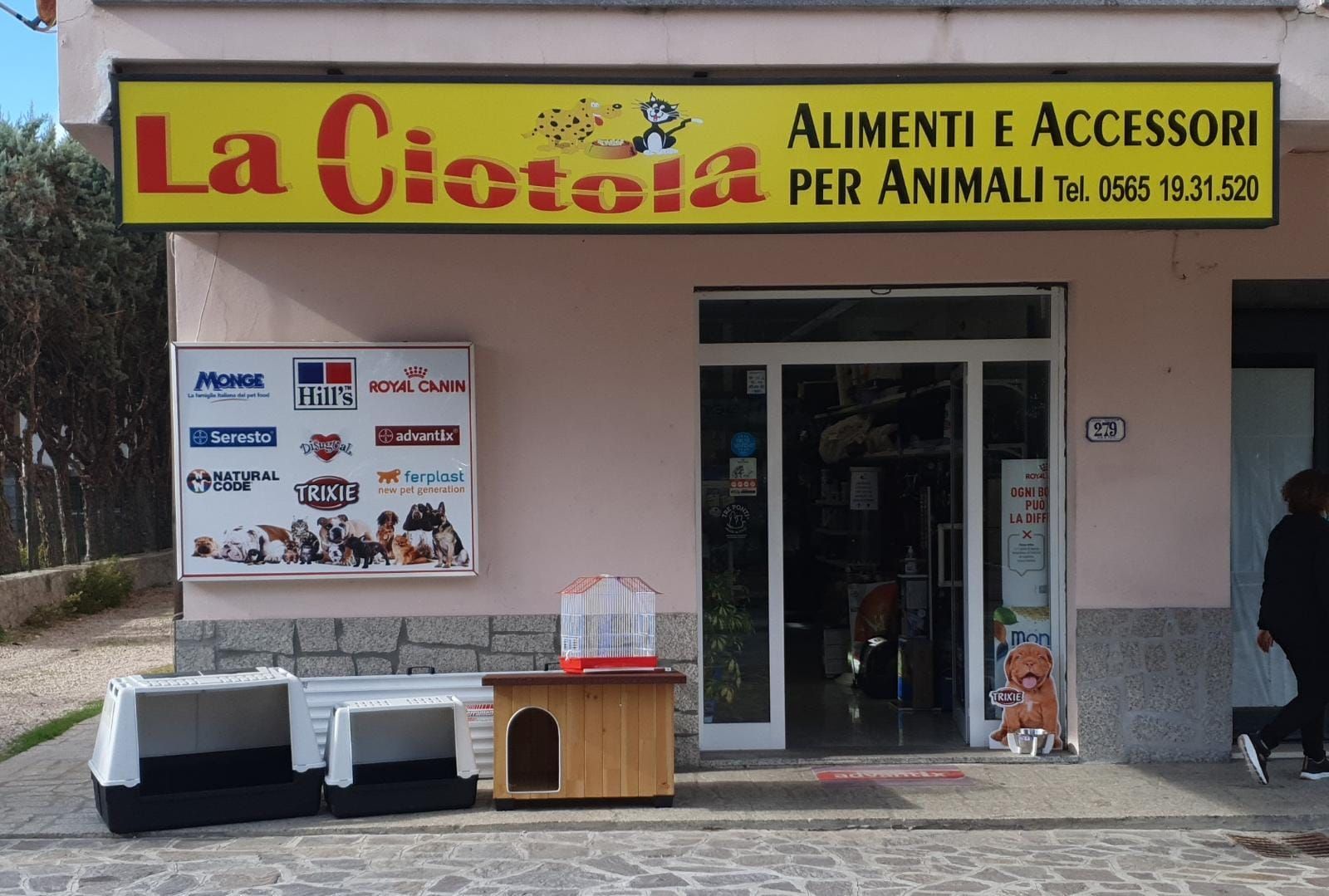 Vetrina di “La Ciotola”, un negozio di alimenti e accessori per animali con un’insegna gialla e tavoli espositivi all’esterno