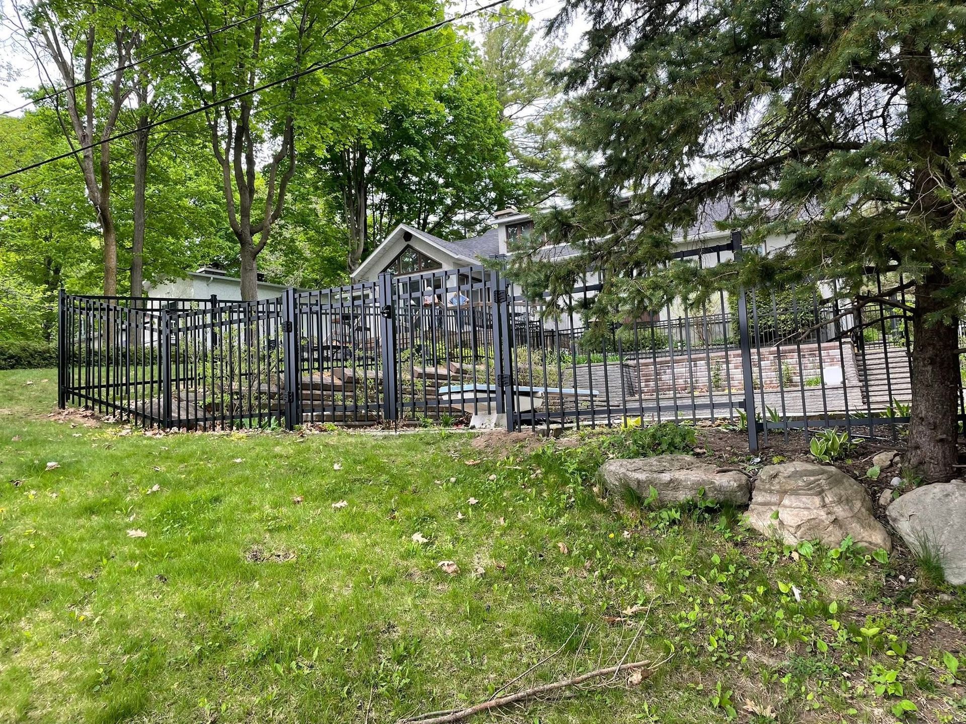 Clôture en fer ornemental noir dans une cour résidentielle arborée