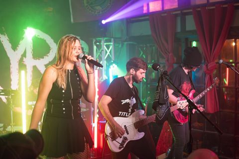 Live band performing onstage under colorful lights, with a singer and two guitarists in a club