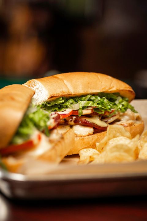 Sandwich with lettuce and tomatoes on a tray, surrounded by potato chips, in a warm restaurant setting