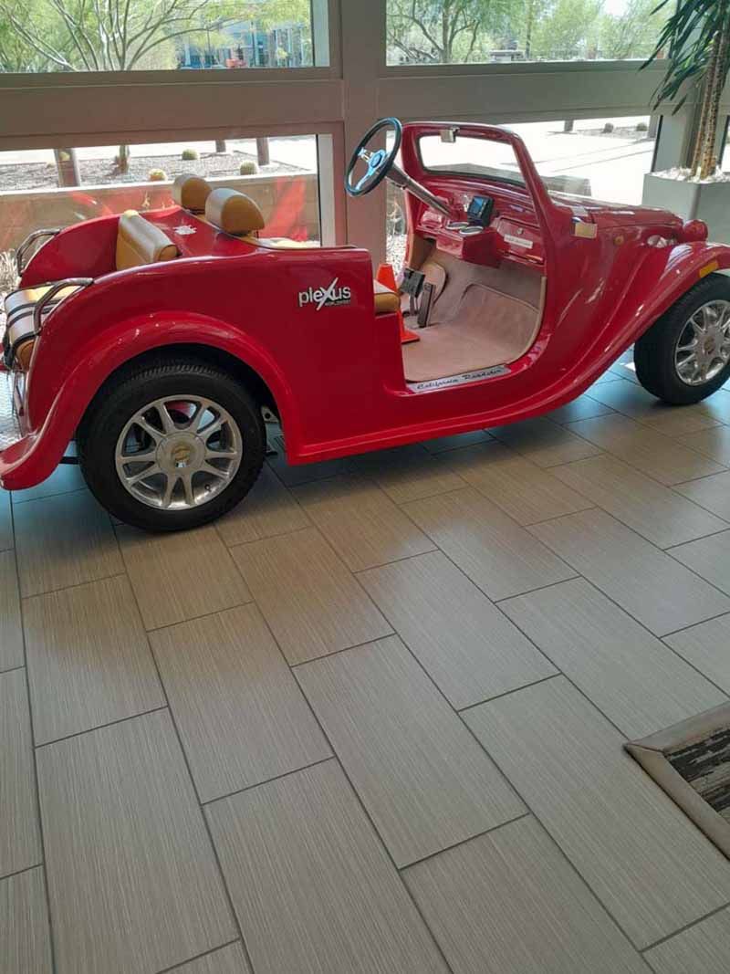 Red toy car parked on a tiled floor near a window; inside an empty room.