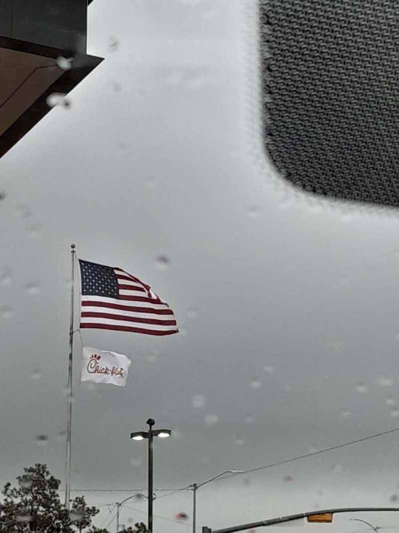 American flag and Chick-fil-A flag flying in front of a cloudy sky.