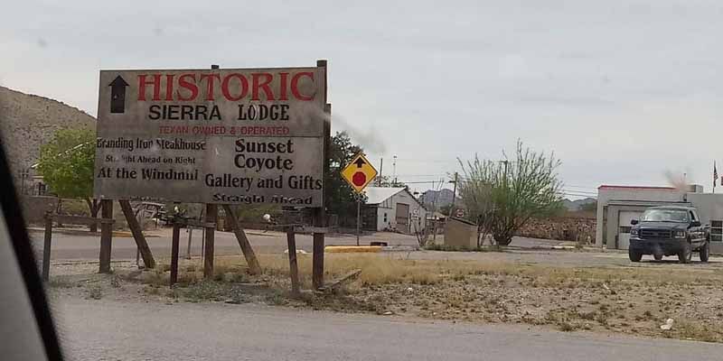 Sign for Historic Sierra Lodge, with arrow, on a dirt road. A pickup truck is in the background.