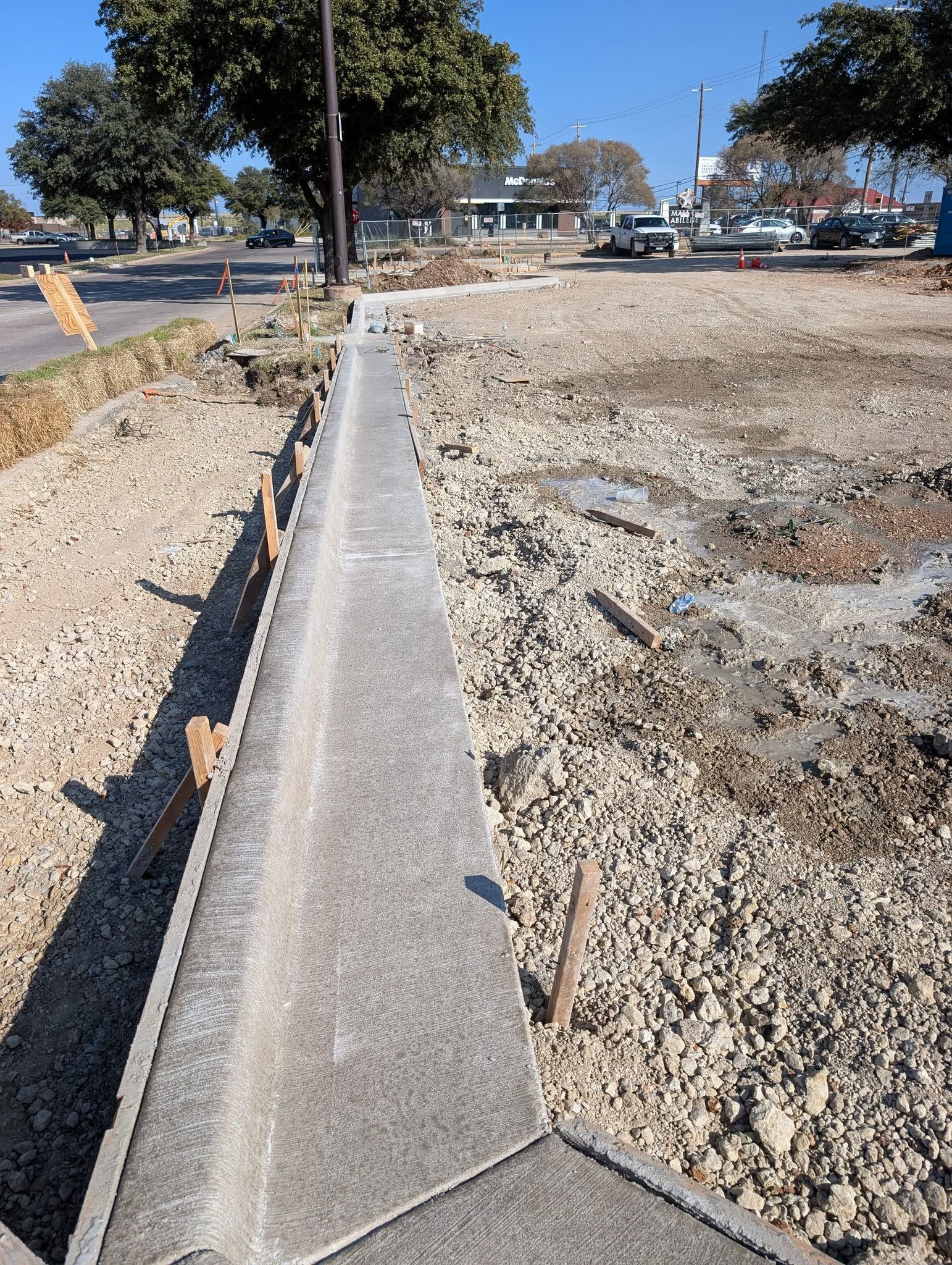 Newly poured concrete curb along a road, with construction materials visible on both sides.