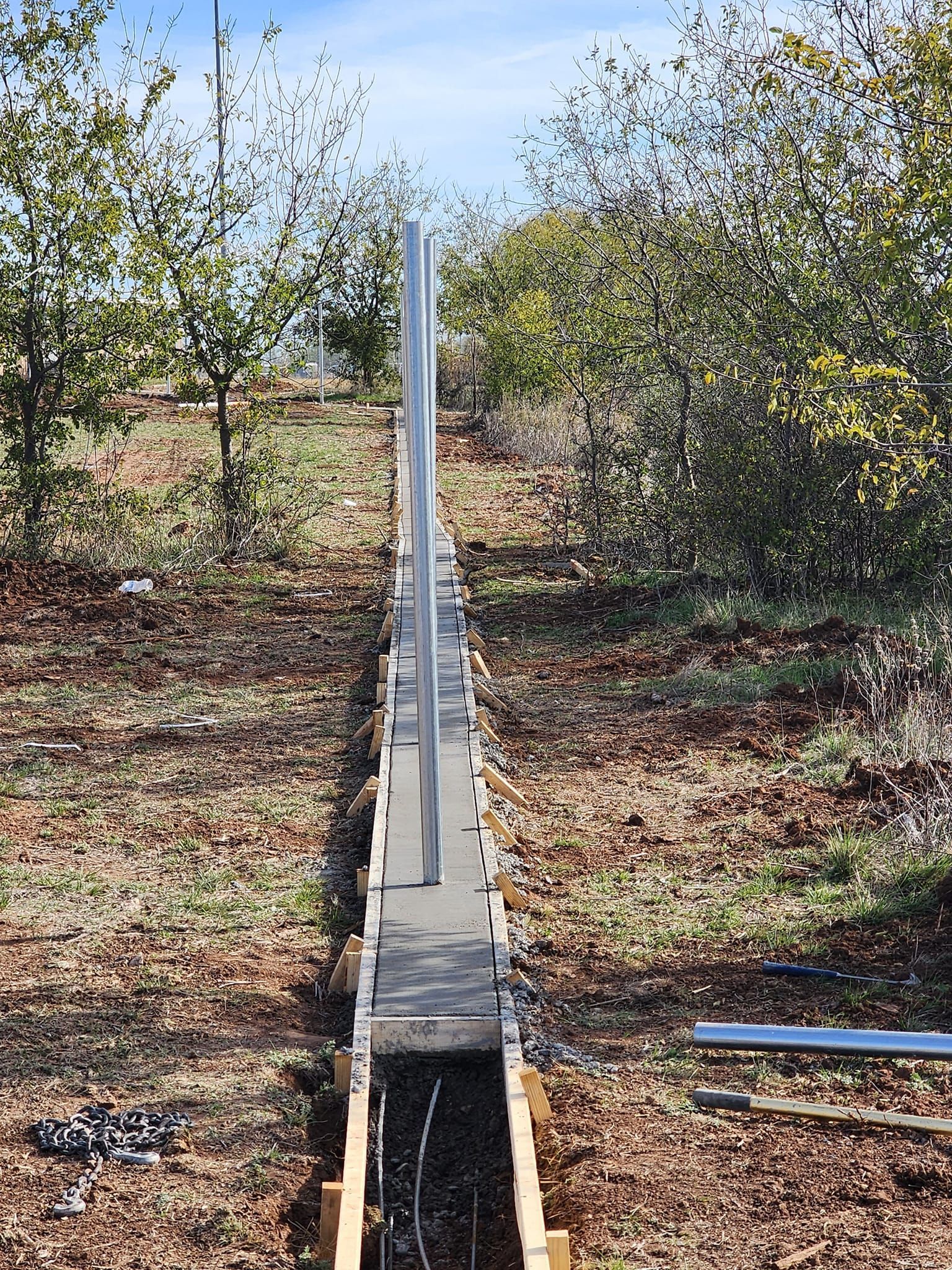 Construction of a concrete foundation with metal posts, likely for a fence, in a wooded area.
