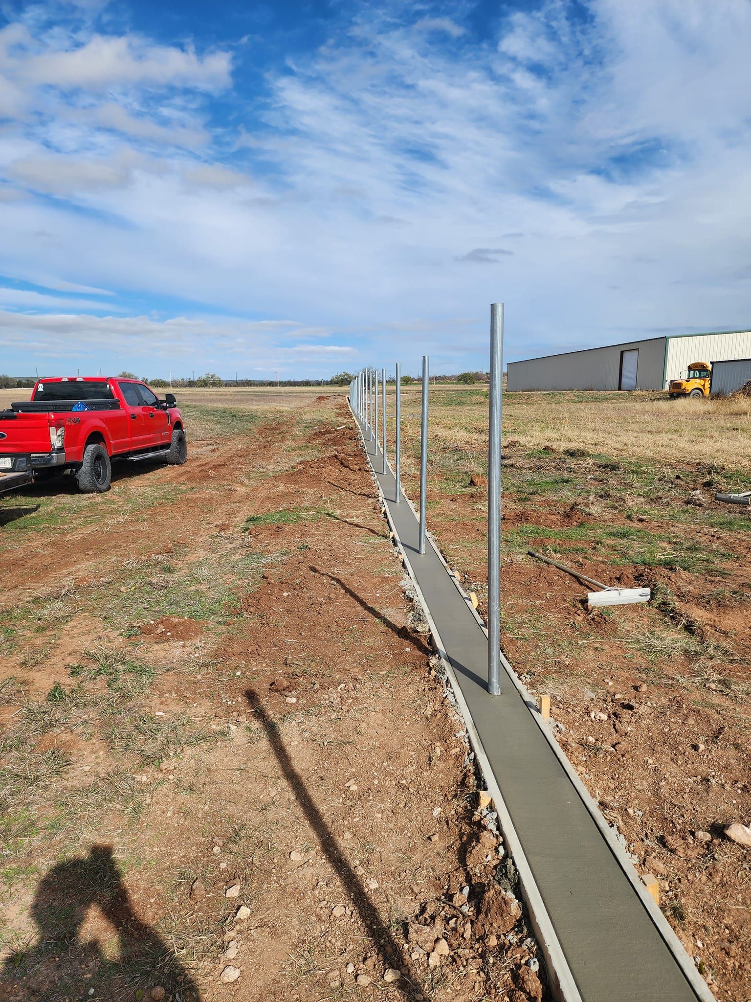 Construction site with concrete base and metal posts; red truck on the left.