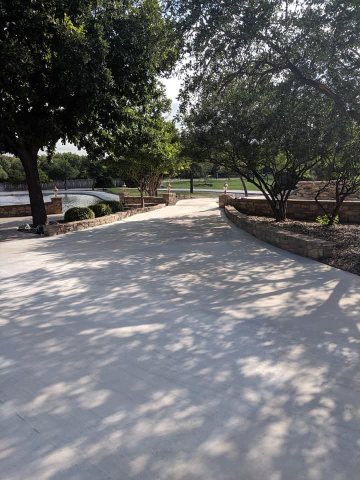 Concrete pathway through a park, lined with trees and stone walls; dappled sunlight.