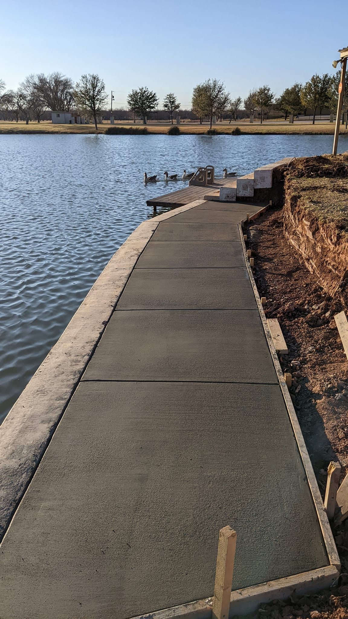 Concrete path leading to a lake, with blue water and trees in the background.