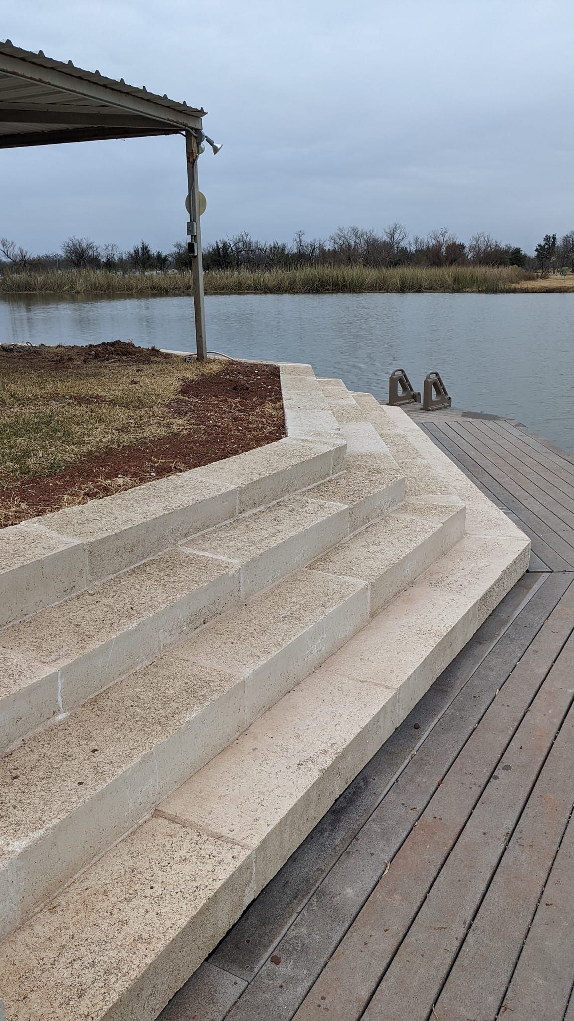 Concrete steps leading down to a body of water with a covered structure on the left and overcast sky.