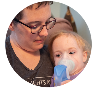 A young mother holding her daughter while she uses a nebulizer.