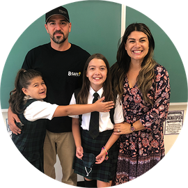 A mom, dad and their two daughter standing in front of a blackboard at school.