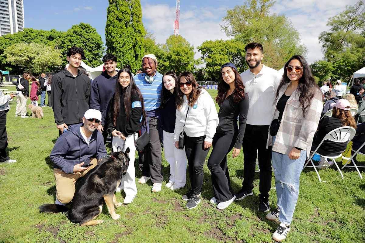 A larger group of walkers and their dog stand in a group outside on a beautiful sunny day at The Walk to Make Cystic Fibrosis History.