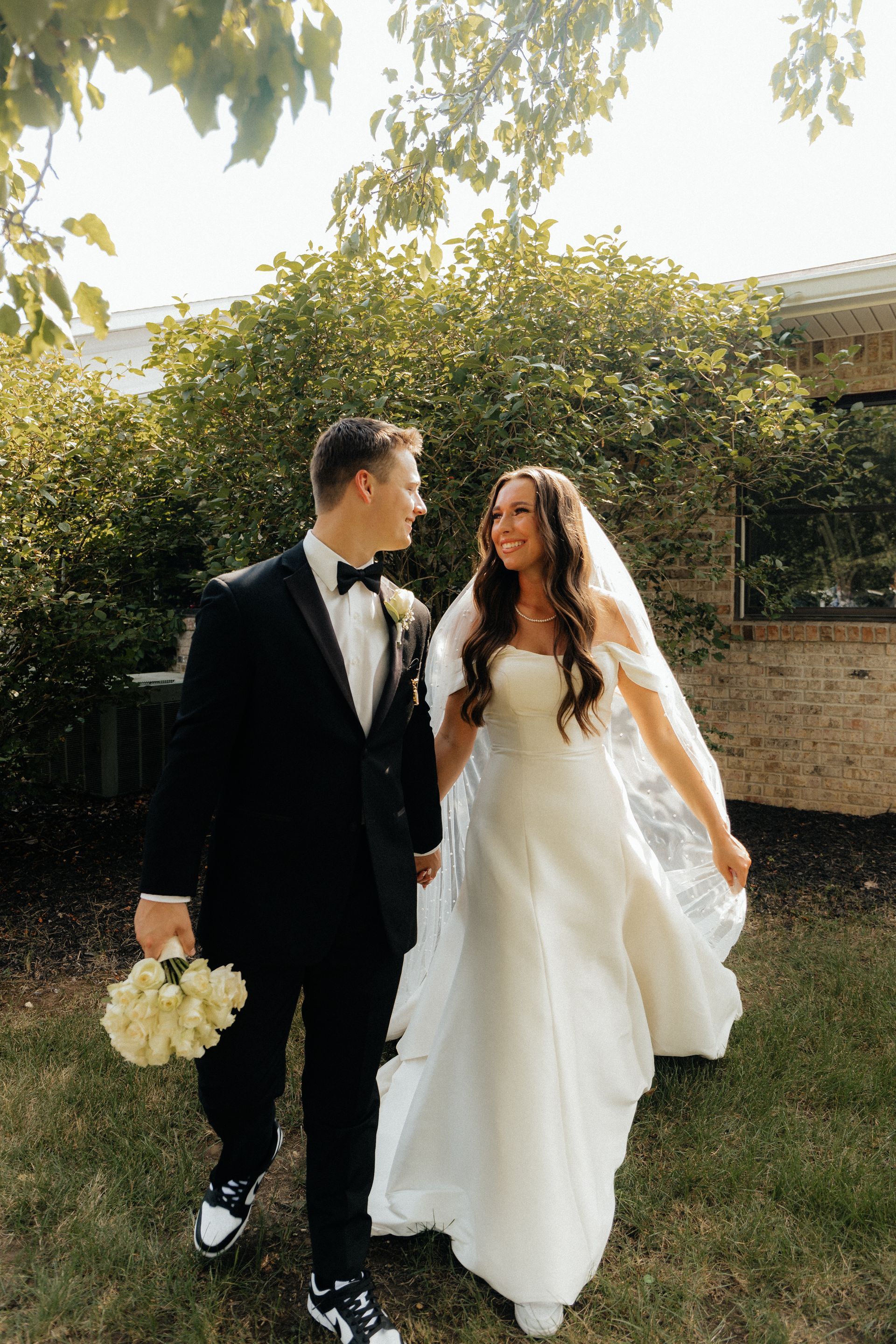 A bride and groom are walking in the grass holding hands.