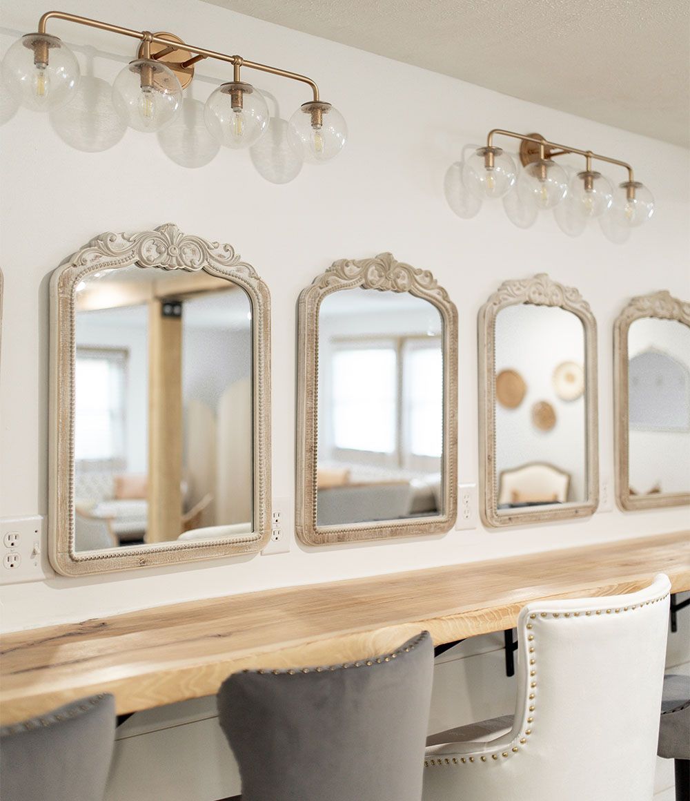 A room with a long wooden table and chairs and mirrors on the wall