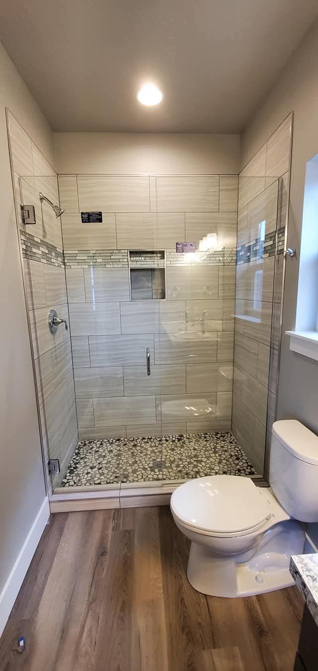 Bathroom with a tiled shower, pebble floor, and a toilet on a wood-look floor.