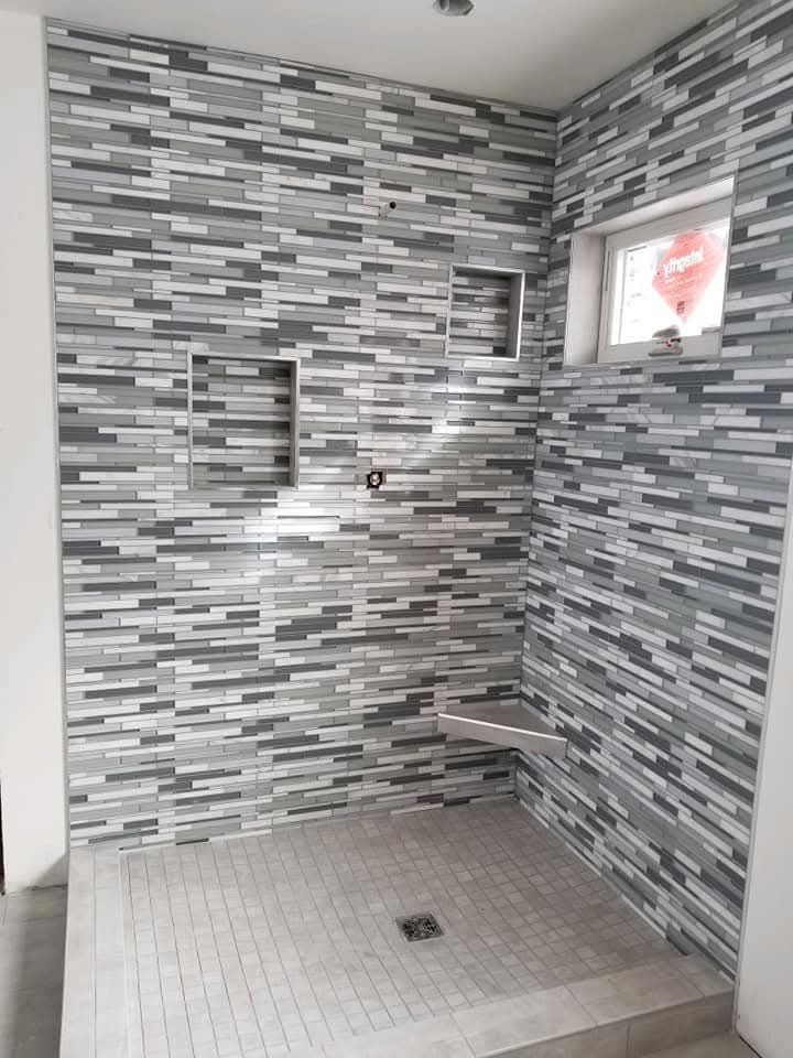 Tiled shower with gray, white, and black mosaic tiles. Includes niches, a bench, and a small window.