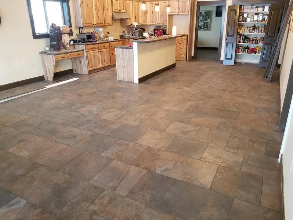 Kitchen with stone tile floor, wood cabinets, and island. Dark stone floor leads to light kitchen.
