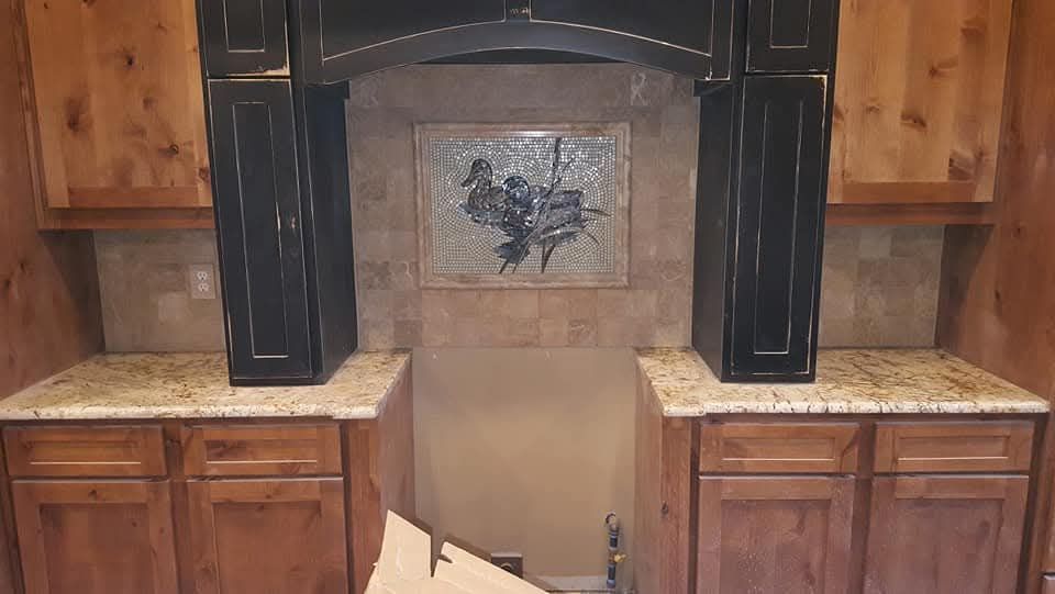 Kitchen cabinets with granite countertops, tile backsplash, and decorative accent in a recessed alcove.