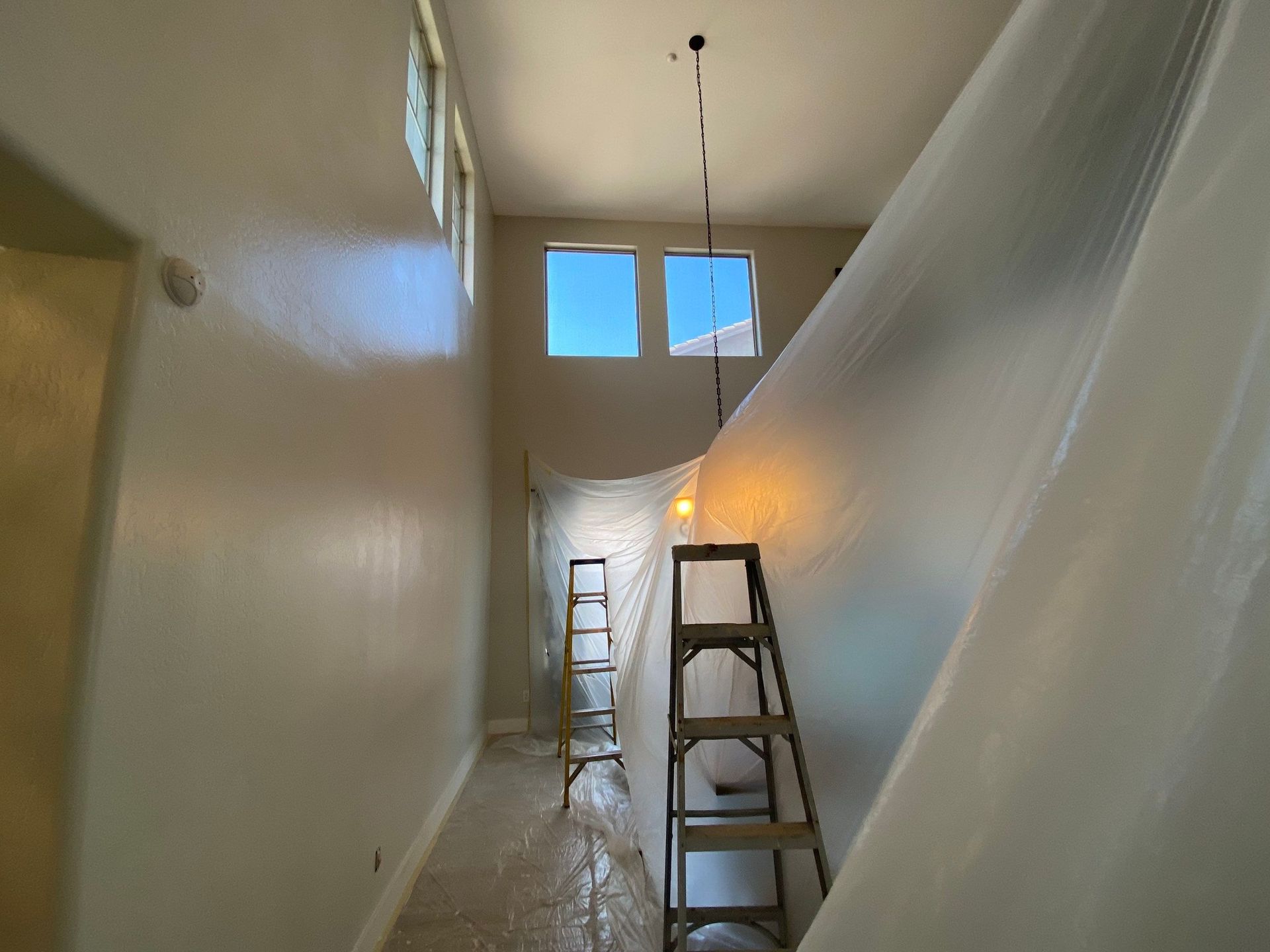 Hallway under construction, covered in plastic sheeting with ladders and windows visible.