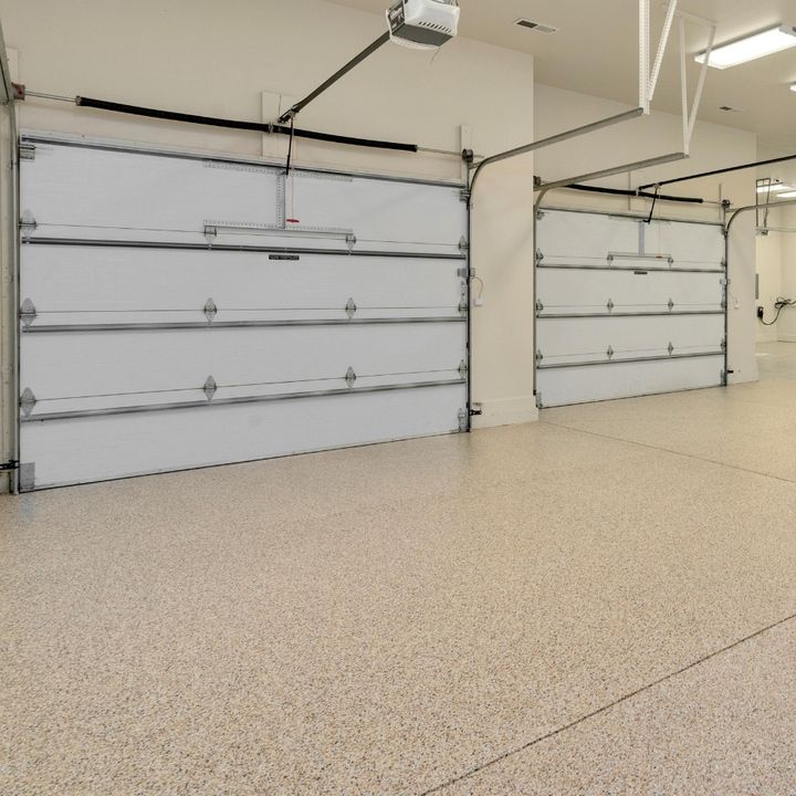 An empty garage with white garage doors and a speckled, beige floor.