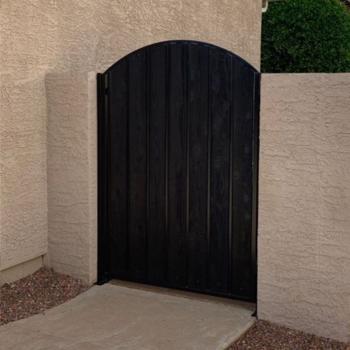 Black arched wooden gate in a stucco wall opening. Concrete path in front.