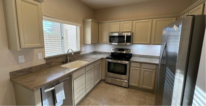 Kitchen with light cabinets, countertops, and stainless steel appliances. Window with blinds.